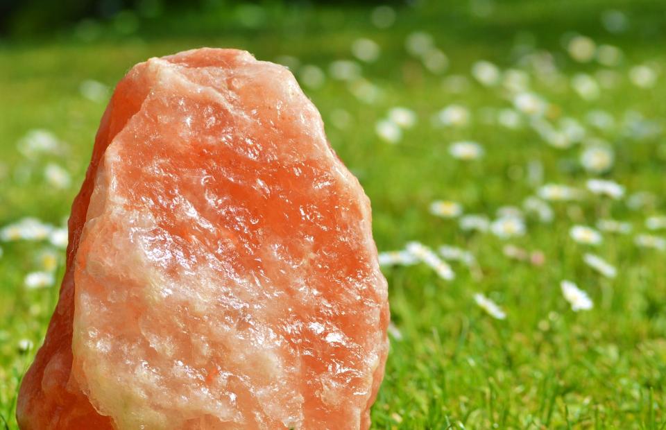 Ein orange schimmernder Steinsalz-Kriztall vor einer grünen Wiese