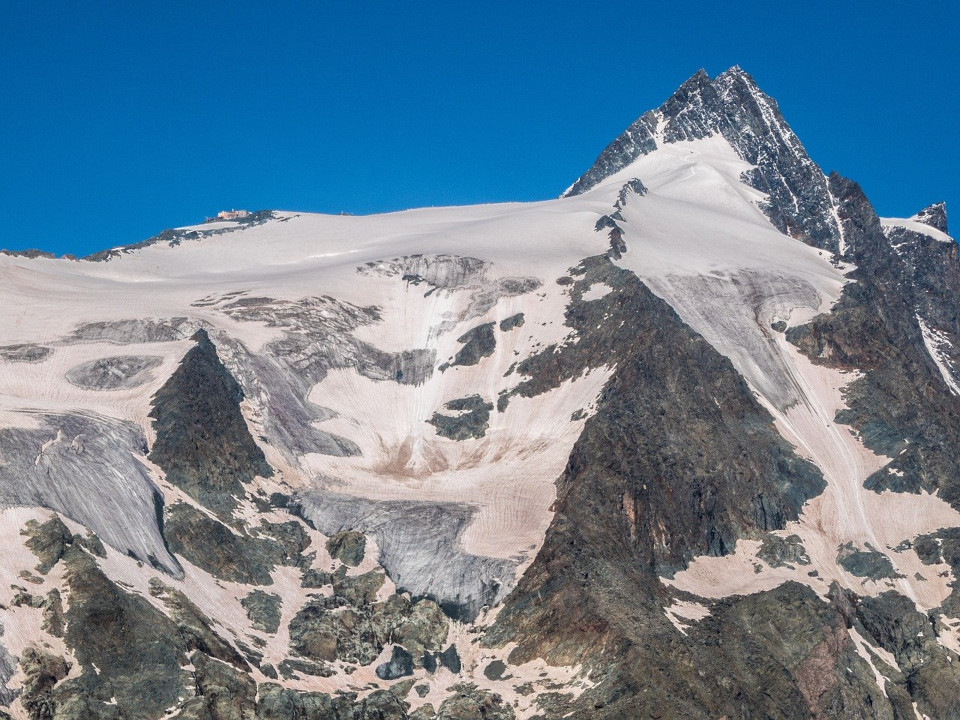 Ein Bild des Großglockners, schneebdeckt und unter wolkenlosem blauen Himmel. 